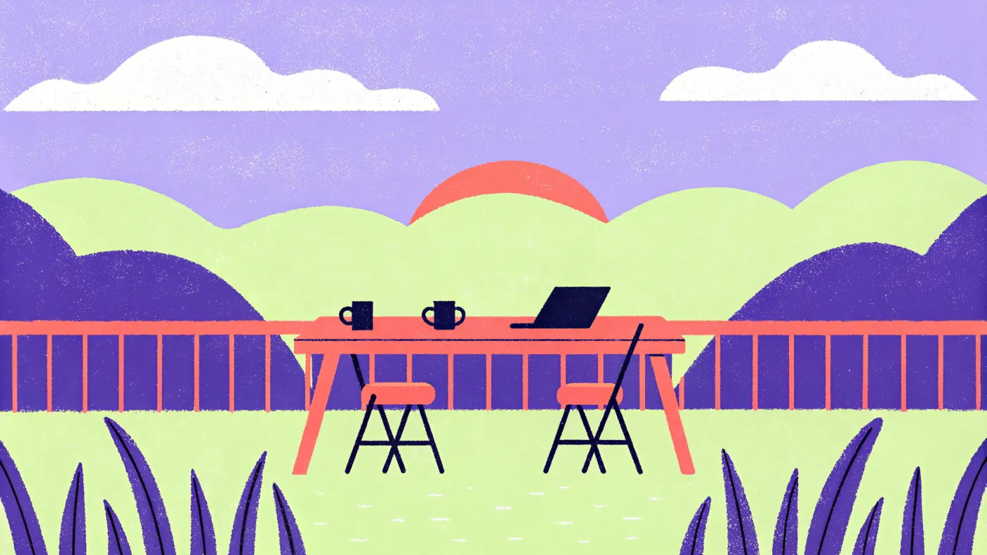 Een lange houten tafel op een terras met een paar laptops, koffiekopjes en een schaal sinaasappels, met de zee op de achtergrond